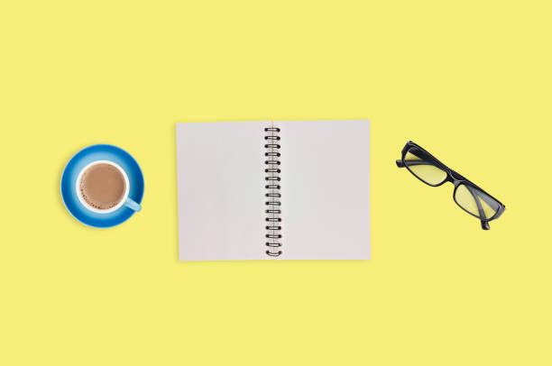 istock One transparent optical glasses in black plastic frame near paper notepad with blank sheets and full cup of coffee on table of yellow color. Top view. Business concept. Copy space for your text 1134881025