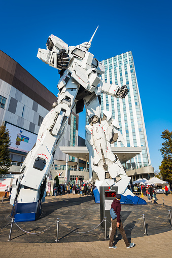 Tourists and shoppers dwarfed by the giant Unicorn Gundam statue outside DiverCity Tokyo Plaza mall on the popular leisure district of Odaiba in Tokyo harbour, Japan.