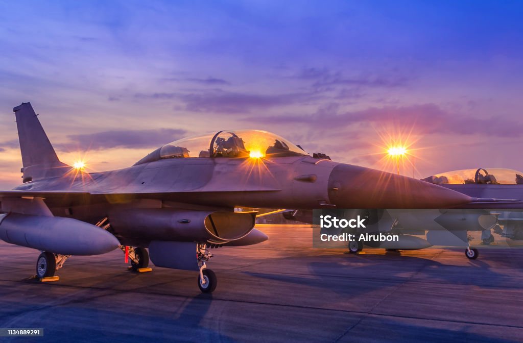 Silhouette fighter jet military aircrafts parked on runway with light airport during air flight show in the night Silhouette fighter jet military aircrafts parked on runway in twilight sunset time with light airport during air flight show in the night Military Base Stock Photo