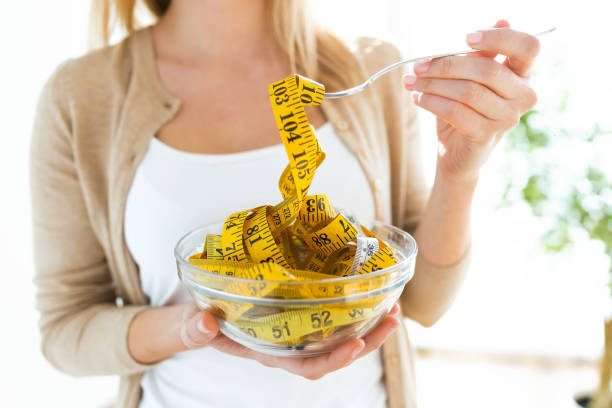 Worried cute woman holding bowl with measuring tapes at home. Worried cute woman holding bowl with measuring tapes at home. diets stock pictures, royalty-free photos & images