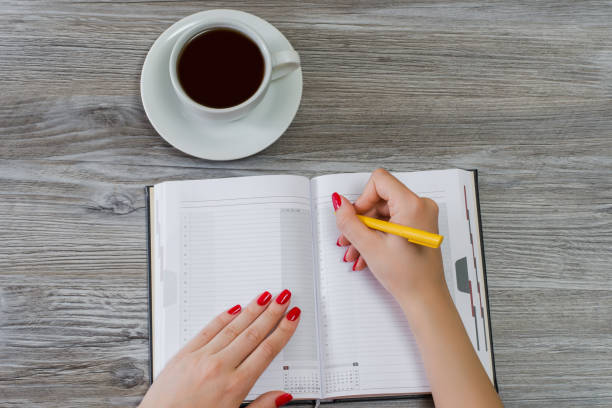 istock Woman's hands writing information in a notepad. Cup of tea is on the background. Overhead view, copy space 1134890213