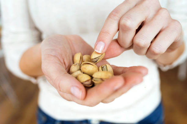 молодая женщина держится за руки и поднимает фисташковые орехи дома. - pistachio стоковые фото и изображения