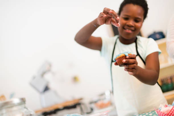 Young African girl sprinkles decoration on cupcake selective focus