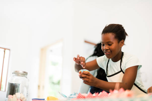 Young African girl decorating cupcakes with sprinkles