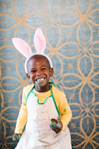 Cute little boy with Easter bunny ears eating candy chocolate egg. Candy all over his face.