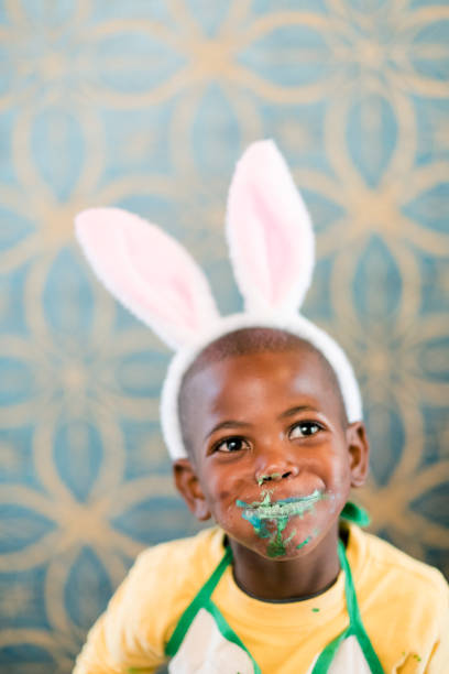 Cute little boy with Easter bunny ears eating candy chocolate egg. Candy all over his face.