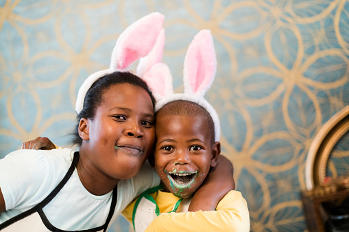 Portraits of girl and boy with bunny ears and mouths full of easter eggs, faces covered with candy.