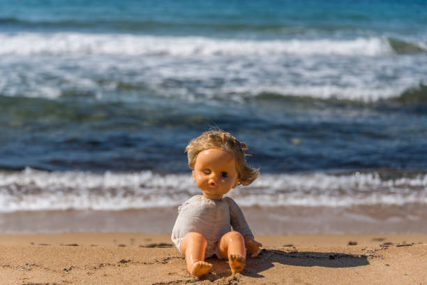 istock Old Broken Toy Doll Sitting on a Beach in Italy 1134905121
