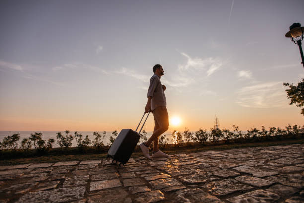 istock Tourist man walking by the sea with suitcase 1134906554