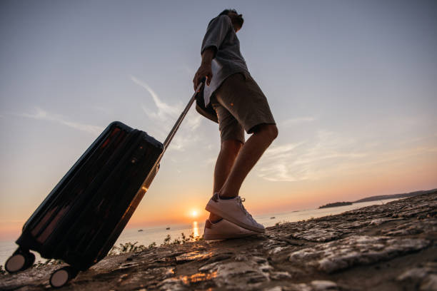 istock Tourist man walking by the sea with suitcase 1134907215