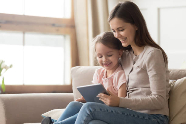 happy mom and kid daughter using digital tablet on sofa - laptop women child digital tablet imagens e fotografias de stock