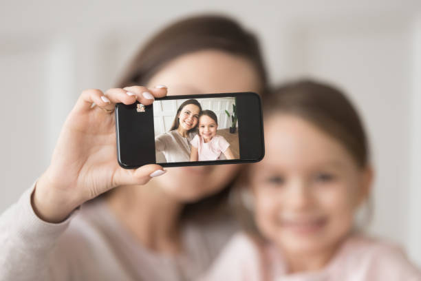 madre feliz sosteniendo teléfono tomar selfie en el celular con la hija - madre fotos fotografías e imágenes de stock
