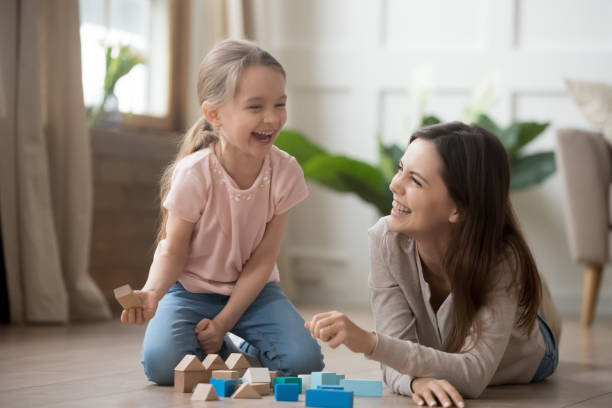 Happy mom and kid daughter laughing playing with wooden blocks Happy family mom baby sitter and little kid daughter laughing playing with wooden blocks sit of warm floor, joyful mother having fun with child girl enjoy funny activity laughter at home together nanny photos stock pictures, royalty-free photos & images