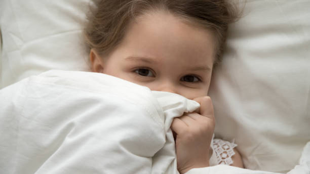 istock Cute kid girl looking at camera under blanket in bed 1134909745