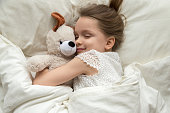 Cute little kid girl hugging teddy bear sleeping in bed