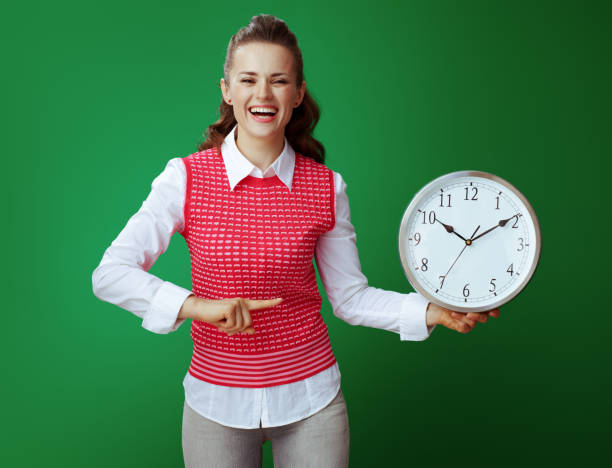 istock smiling student pointing at white round clock isolated on green 1134910523