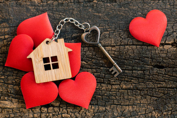 House key in heart shape with home keyring on wood background decorated with mini hearts, copy space stock photo