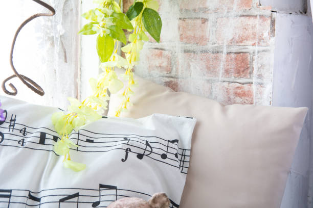 Pillow with musical notes on the windowsill with flowers. Brick wall background with artificial flowers