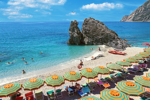 Beautiful beach popular tourist small town of Monterosso in the Cinque Terre Park. The beautiful sandy beach in Italy. Seascape. Striped beach umbrellas on the shore of the Mediterranean sea. Romantic place.