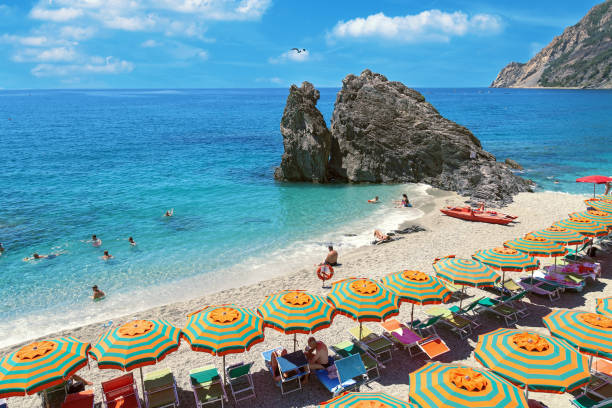 Beautiful beach popular tourist small town of Monterosso in the Cinque Terre Park in Italy. Seascape. Romantic place. Beautiful beach popular tourist small town of Monterosso in the Cinque Terre Park. The beautiful sandy beach in Italy. Seascape. Striped beach umbrellas on the shore of the Mediterranean sea. Romantic place. liguria photos stock pictures, royalty-free photos & images