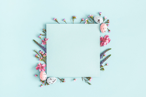 Easter composition. Easter eggs, flowers, paper blank on pastel blue background. Flat lay, top view, copy space