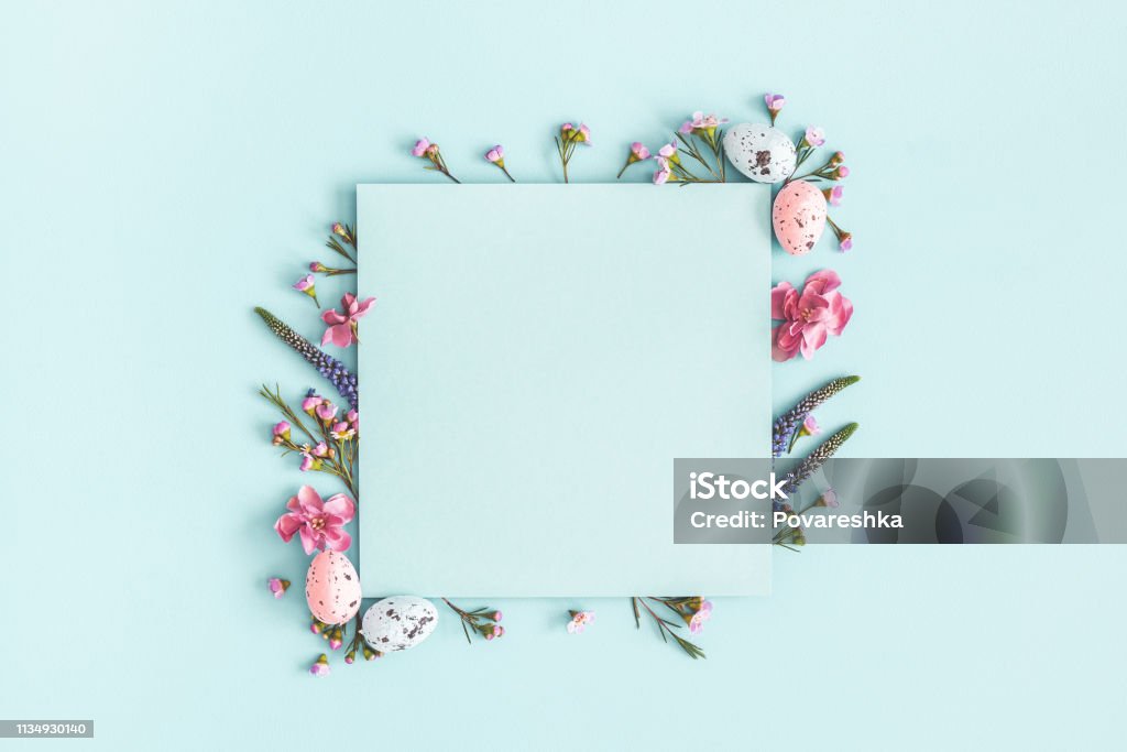 Easter composition. Easter eggs, flowers, paper blank on pastel blue background. Flat lay, top view, copy space Easter Stock Photo