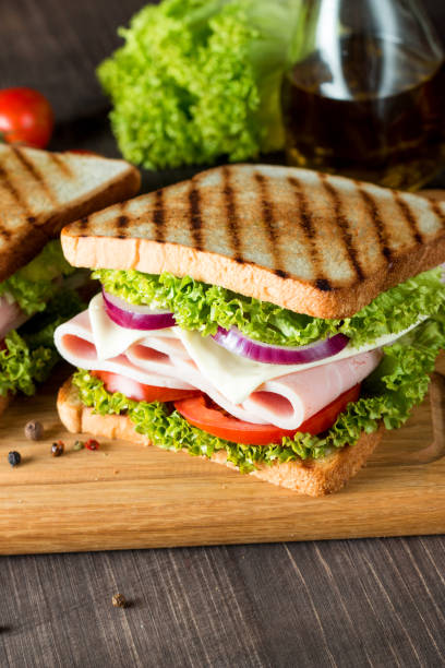 close-up photo of a club sandwich. sandwich with meat, prosciutto, salami, salad, vegetables, lettuce, tomato, onion and mustard on a fresh sliced rye bread on wooden background. olives background. - sandwich club sandwich ham turkey imagens e fotografias de stock