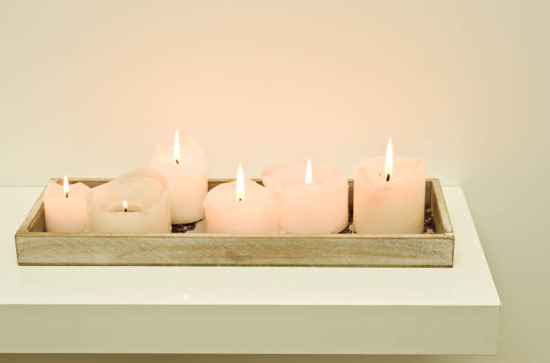 Elegant lit candles standing on a shelf against white wall, home decoration.