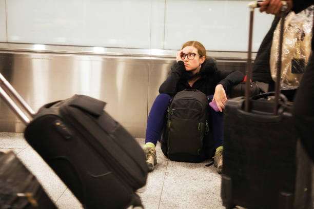 Distraught woman sits in airport while travelers pass her stock photo