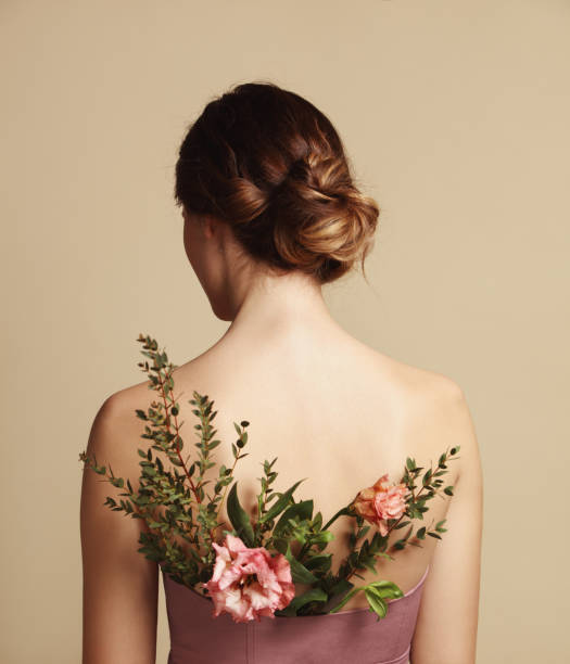 Rear view of young woman and flowers Portrait of woman with flowers behind her back hair bun stock pictures, royalty-free photos & images
