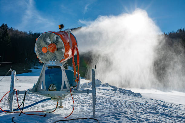 Snow machine blowing artificial snow over a ski slope on a sunny day Snow machine blowing artificial snow over a ski slope on a sunny day fake snow stock pictures, royalty-free photos & images