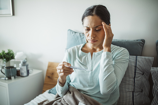 Woman with flu in bed, she use thermometer to measure temperature