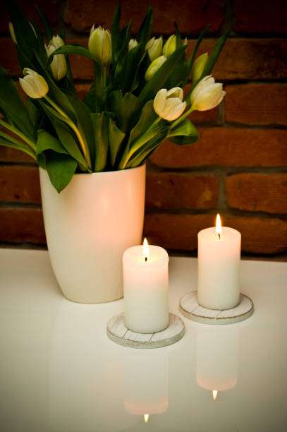 istock White tulips bouquet in a vase against red brick wall and candles. 1134953012
