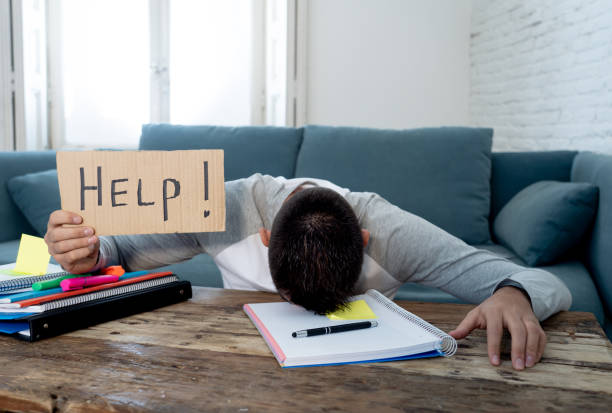 Young tired and stressed student working on his homework, masters feeling desperate and frustrated asking for help. In over Education, learning difficulties, finals exams and emotional stress concept. stock photo