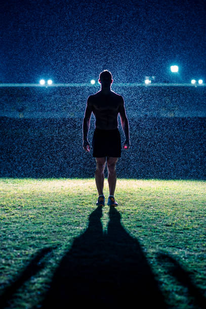 silhouette of strong male athlete standing in front of stadium in the rain at night - doping imagens e fotografias de stock