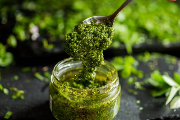 pesto sauce in a spoon, jar with pesto sauce pesto sauce in a spoon, jar with pesto sauce savory sauce stock pictures, royalty-free photos & images