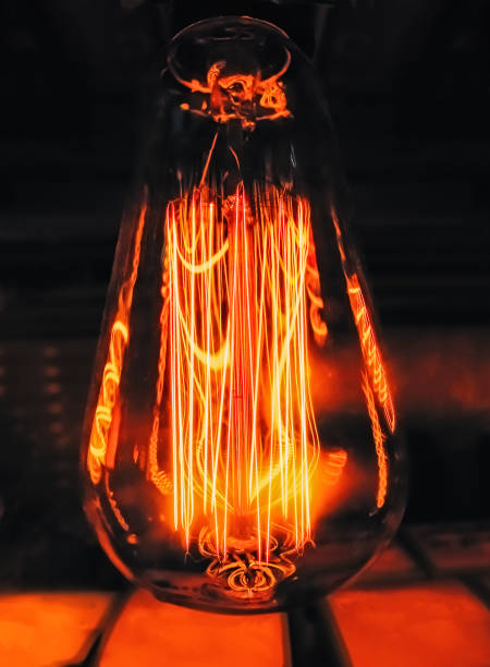 istock Bright glowing clear glass lamp pear shaped close up. Illumination Edison retro lamp dark background. Antique vintage filament light bulb. 1134961781