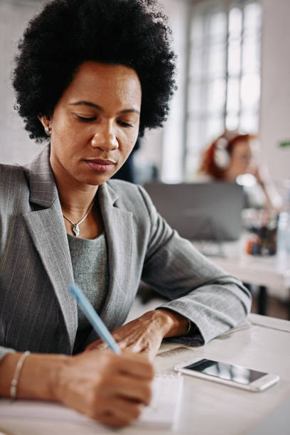 istock Black female entrepreneur taking notes while sitting at her office desk. 1134967582