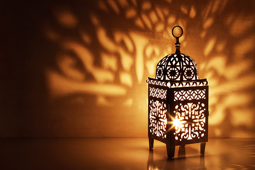 Silhouette of Moroccan ornamental lantern with burning glowing candle. Decorative shadows. Festive greeting card, invitation for Muslim holy month Ramadan Kareem, festive night background.