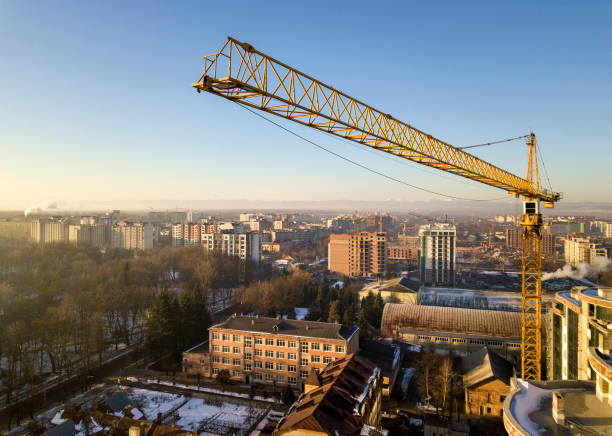 Apartment or office tall building under construction, top view. Tower crane on bright blue sky copy space background, city landscape stretching to horizon. Drone aerial photography.