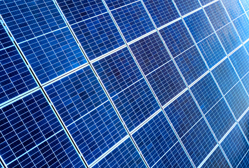 Close-up surface of lit by sun blue shiny solar photo voltaic panels. System producing renewable clean energy. Renewable ecological green energy production concept.