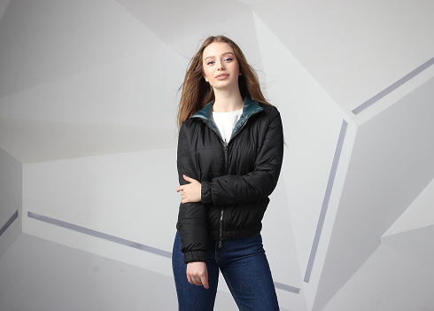 Young girl girl wearing black jacket with area for your logo, mock-up of white women hoodie, on modern wall 
 background