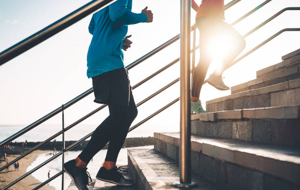 vista de los corredores piernas entrenamiento al aire libre-pareja joven haciendo una sesión de entrenamiento en las escaleras junto a la playa al atardecer-gente sana, jogging y el concepto de estilo de vida deportiva - jumping women running vitality fotografías e imágenes de stock