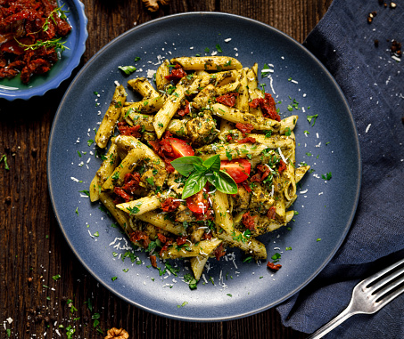 Penne pasta with spinach, sun dried tomatoes and chicken, sprinkled with parmesan cheese and fresh parsley  on a ceramic plate on a wooden rustic table, top view