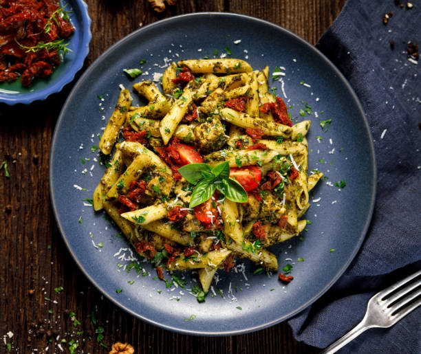 massa de penne com espinafre, tomates secos do sol e galinha, polvilhado com queijo do parmesão e salsa fresca em uma placa cerâmica - rigatoni - fotografias e filmes do acervo