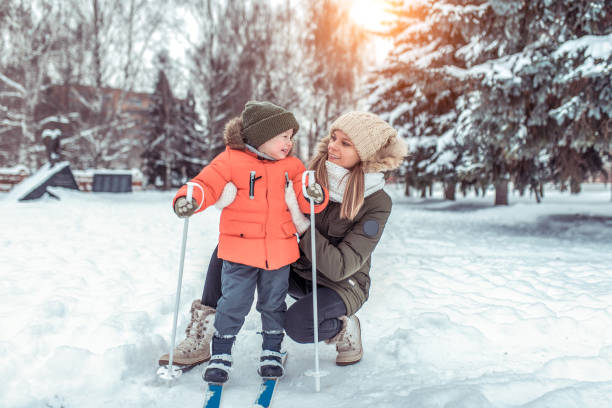 eine junge frau, mutter unterstützt mit sorgfalt, kleiner junge sohn 3-6 jahre alt, skiwinter im waldpark. der erste sportunterricht auf der straße. fröhlich lächelnd spielen mit kind. freiraum für text. - ski resort hut snow winter stock-fotos und bilder