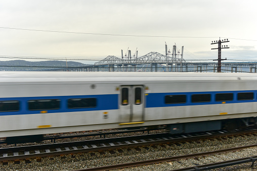 The new Tappan Zee bridge under construction across the Hudson River in New York across train tracks as a train passes by.