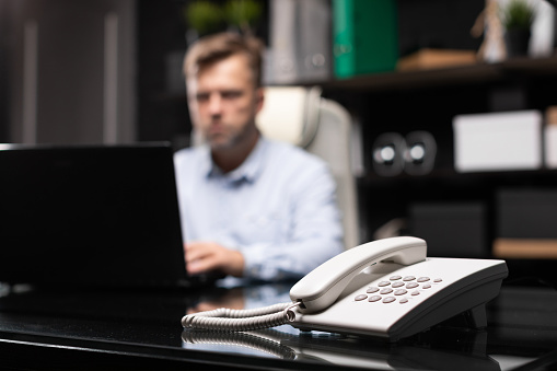 White landline phone close-up isolated. busy man works in stylish office with laptop. Portrait of businessman at work. Business concept in modern world. Photo with depth of field