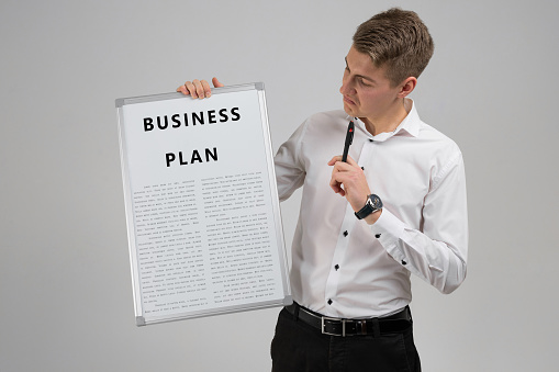 Portrait of a young man in a white shirt with a business plan and a pen in his hands isolated in a bright Studio. Business plan strategy with presentation. Business concept