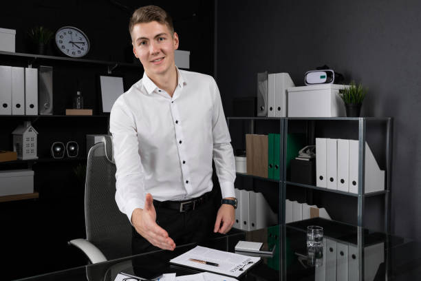 young man says Hello standing at table in bright office young Man in white shirt standing near table in office. Business concept in modern world man writing on white board stock pictures, royalty-free photos & images